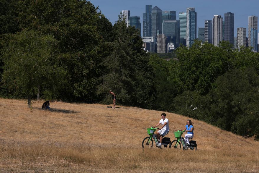 People ride bicycles in Greenwich Park amid dried grass in London, Tuesday, Aug. 11, 2026. (AP Photo/Kin Cheung)