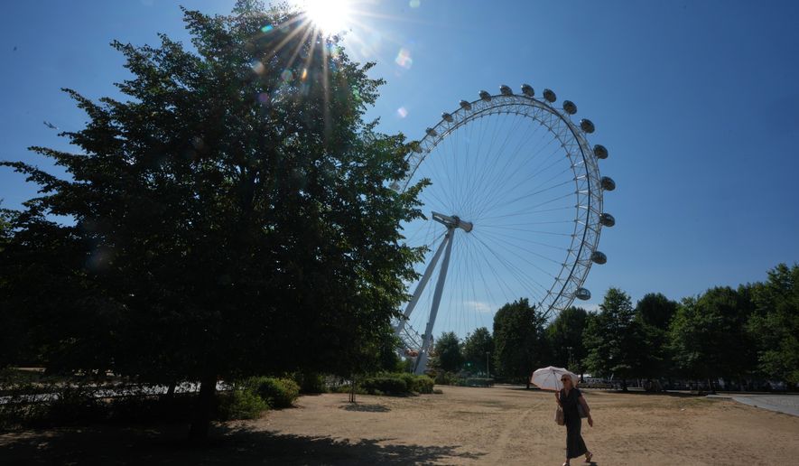 A woman shades under an umbrella as she walks past the London Eye during the fifth heatwave of the year in London, Thursday, Aug. 13, 2026. (AP Photo/Kirsty Wigglesworth)