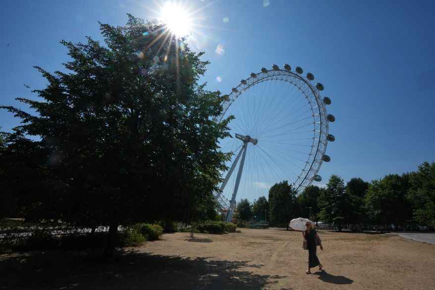 A woman shades under an umbrella as she walks past the London Eye during the fifth heatwave of the year in London, Thursday, Aug. 13, 2026. (AP Photo/Kirsty Wigglesworth)