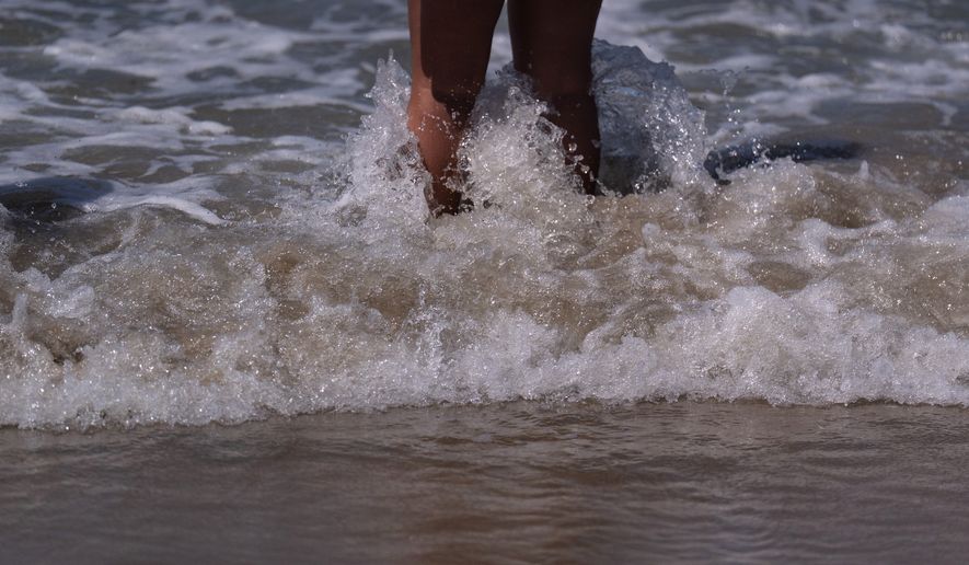 A beachgoer stands in shallow water at Bolsa Chica State Beach in Huntington Beach, Calif., Friday, July 24, 2026. (AP Photo/Jae C. Hong)