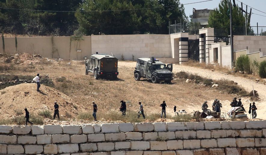 Israeli soldiers stand guard next to settlers in front of Palestinian homes that they have blockaded in the village of Qusra, south of Nablus, in the occupied West Bank, Wednesday, Aug. 12, 2026. (AP Photo/Nidal Eshtayeh)