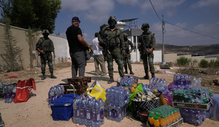 Activists accumulate food and water supplies in front of Israeli army soldiers who are blocking the road leading to the houses of three Palestinian families that have been besieged by Israeli settlers for six days, in the occupied West Bank village of Qusra, south of Nablus, Friday, Aug. 14, 2026. (AP Photo/Majdi Mohammed)