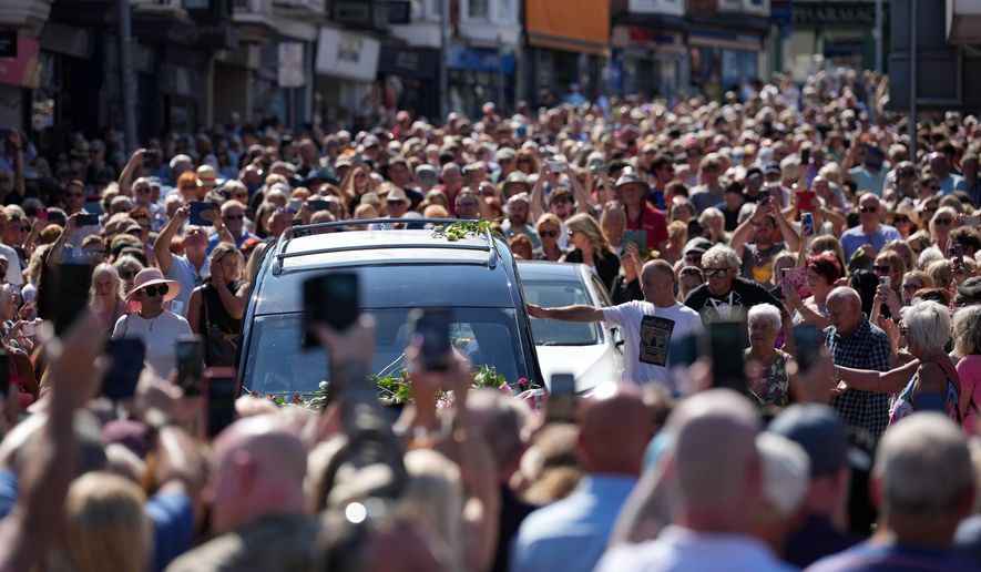 Fans of singer Bonnie Tyler line the streets as her coffin is transported in a hearse back to her former home ahead of her funeral, in Mumbles, Wales, Saturday, Aug. 15, 2026. The Total Eclipse Of The Heart musician, whose real name was Gaynor Hopkins, died in hospital in Portugal on July 8 at the age of 75. (AP Photo/Alastair Grant)