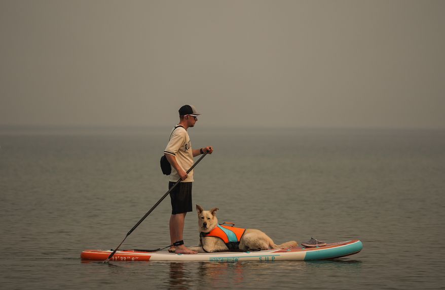 A man paddleboards with a dog as smoke from the Bald Range wildfire envelopes Okanagan Lake, in Penticton, B.C., on Sunday, Aug. 9, 2026. (Darryl Dyck/The Canadian Press via AP)