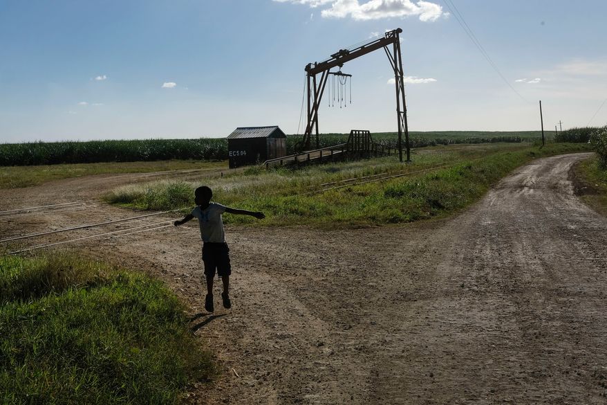 FILE - A youth plays near the machine where the sugar cane is weighed in the Lima batey, or neighborhood, in La Romana, where Central Romana Corporation, Ltd. operates its sugar operations in Dominican Republic, Nov. 17, 2021. (AP Photo/Matias Delacroix, File)