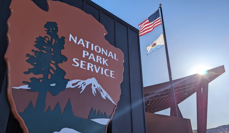 National Park Service sign on the front of the Joshua Tree Visitor Center with an American flag in the background. File photo credit: Leigh Trail via Shutterstock.
