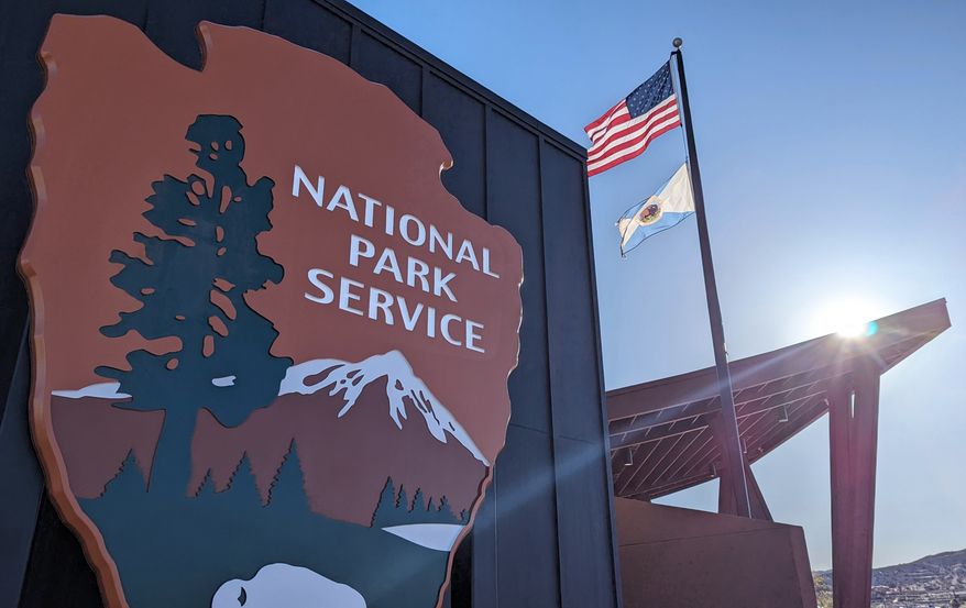National Park Service sign on the front of the Joshua Tree Visitor Center with an American flag in the background. File photo credit: Leigh Trail via Shutterstock.
