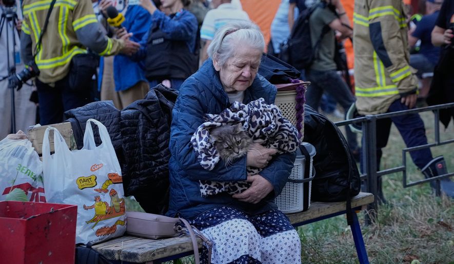 An elderly woman holds her car as she sits with her belongings in front of heavily damaged residential buildings after an overnight Russian attack, in Kyiv, Ukraine, Thursday, Aug. 20, 2026. (AP Photo/Efrem Lukatsky)