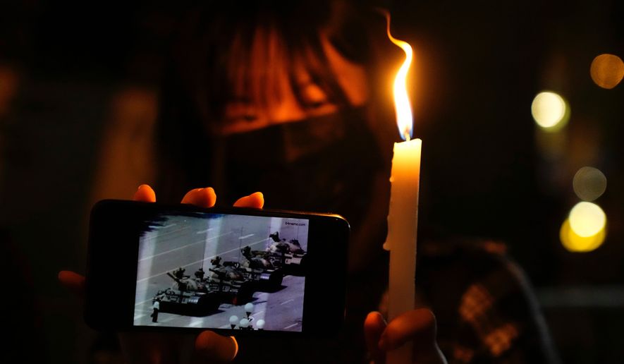 FILE -A woman holds up a candle and an image of a man facing off tanks to mark the anniversary of the military crackdown on a pro-democracy student movement in Beijing, during a light candle vigil outside Victoria Park in Hong Kong, Friday, June 4, 2021. (AP Photo/Kin Cheung, File, File)