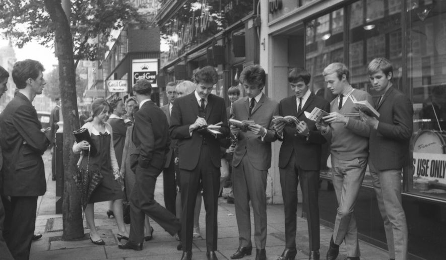 The five members of The Hollies, an in-the-charts beat group, autographing and examining copies of their new book How To Run a Beat Group, outside a music shop on Charing Cross Road where the book is being sold on Monday, Aug. 17, 1964 in London, England. (AP Photo/Robert Dear)