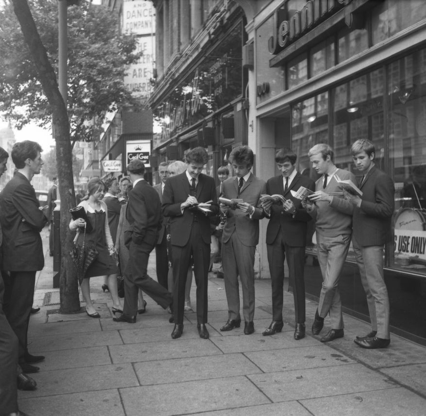 The five members of The Hollies, an in-the-charts beat group, autographing and examining copies of their new book How To Run a Beat Group, outside a music shop on Charing Cross Road where the book is being sold on Monday, Aug. 17, 1964 in London, England. (AP Photo/Robert Dear)