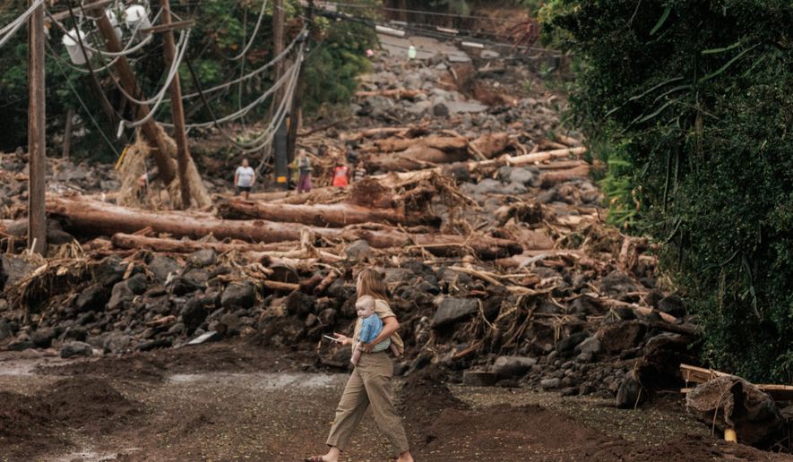 A woman and child walk past a debris-strewn street in Naalehu, Hawaii, Monday, Aug. 17, 2026, after a severe weather system went through the area. (Stephen Lam/San Francisco Chronicle via AP)