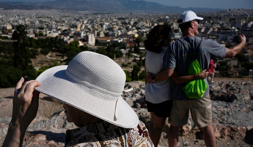 Tourists wearing hats take photographs on the rocky Areios Pagos Hill next to the Acropolis in Athens, Greece, Friday, Aug. 14, 2026. (AP Photo/Thanassis Stavrakis)