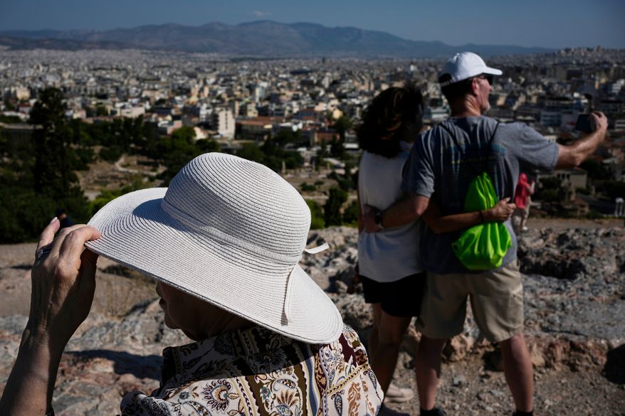 Tourists wearing hats take photographs on the rocky Areios Pagos Hill next to the Acropolis in Athens, Greece, Friday, Aug. 14, 2026. (AP Photo/Thanassis Stavrakis)