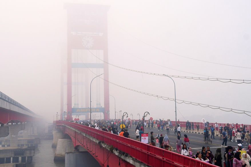 People walk along the Ampera Bridge as haze from wildfires blankets the city of Palembang, in South Sumatra, Indonesia, Sunday, Aug. 23, 2026. (AP Photo/Muhammad Fajri)