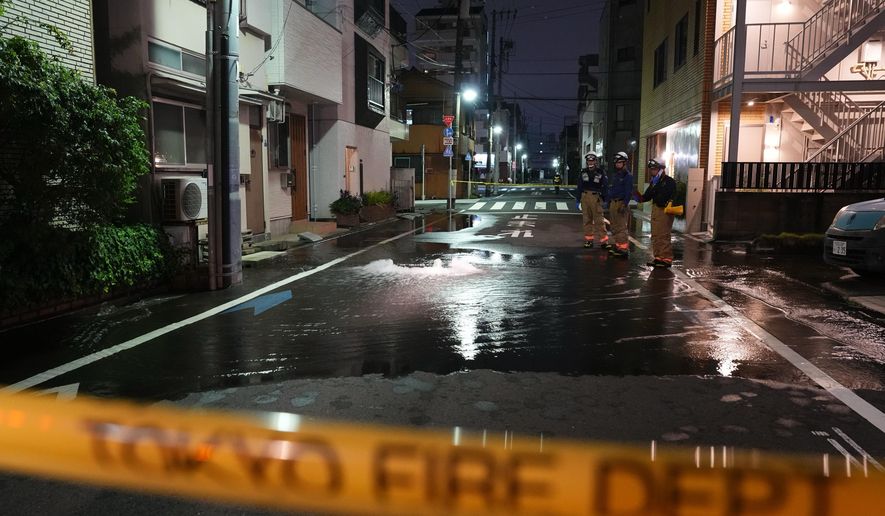 First responders from the Tokyo Fire Department stand on a street partially flooded in the early hours of Sunday, Aug. 23, 2026, following the rupture of a water pipe after an earthquake that struck the area and neighboring prefectures. (Kazuki Kozaki/Kyodo News via AP)