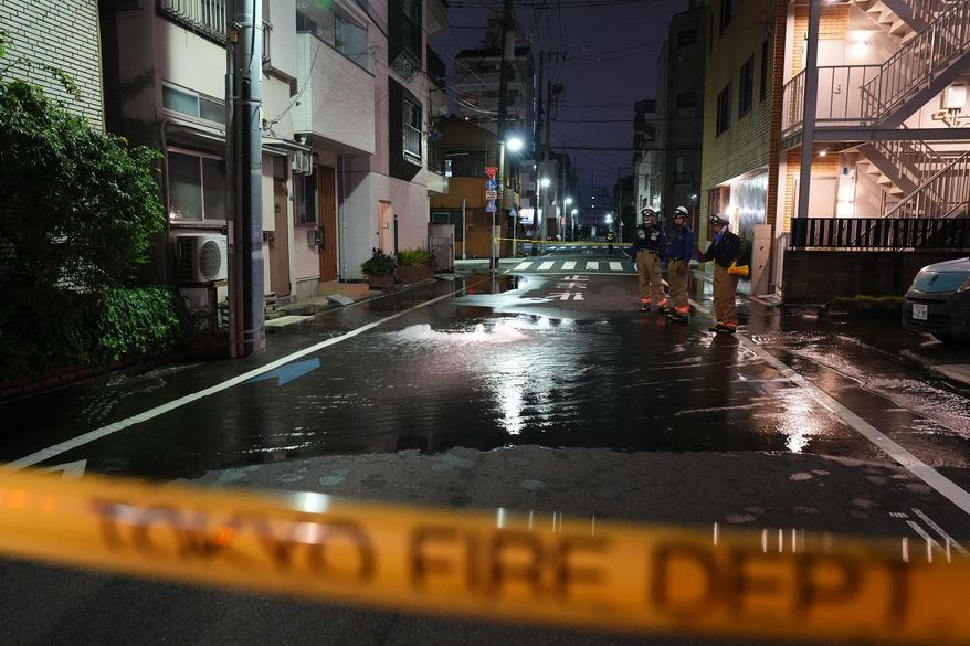 First responders from the Tokyo Fire Department stand on a street partially flooded in the early hours of Sunday, Aug. 23, 2026, following the rupture of a water pipe after an earthquake that struck the area and neighboring prefectures. (Kazuki Kozaki/Kyodo News via AP)