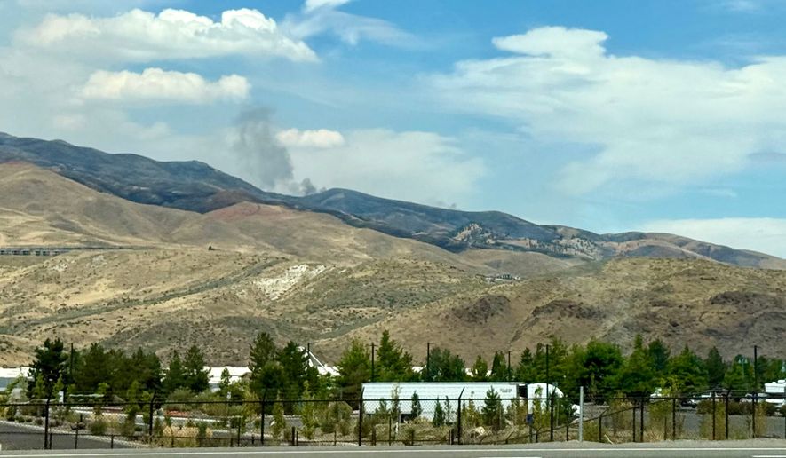 Smoke billows in the distance as a wildfire in Reno, Nev., destroyed homes and caused thousands to evacuate their homes, Sunday, August 23, 2026. (AP Photo/Haven Daley)