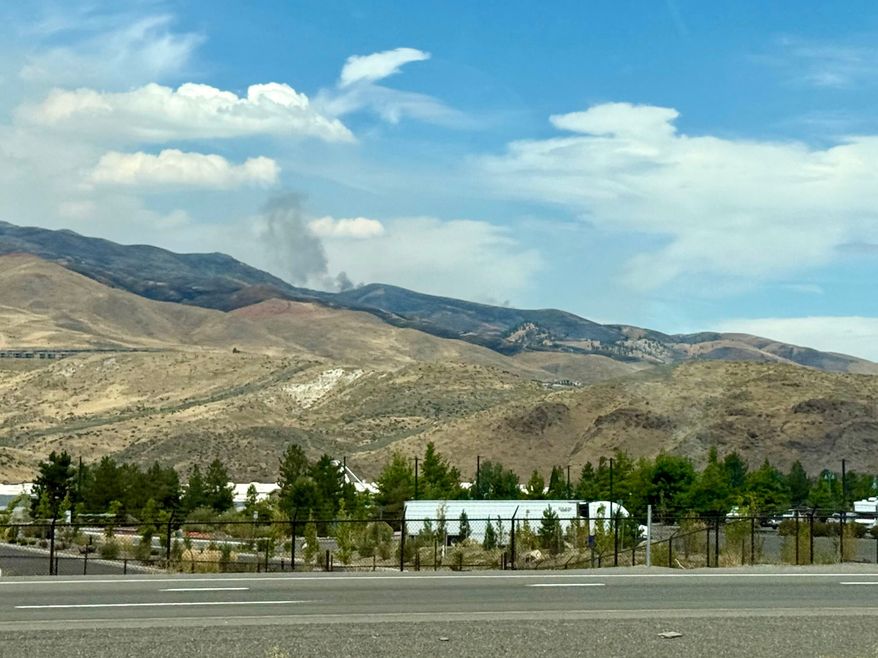 Smoke billows in the distance as a wildfire in Reno, Nev., destroyed homes and caused thousands to evacuate their homes, Sunday, August 23, 2026. (AP Photo/Haven Daley)