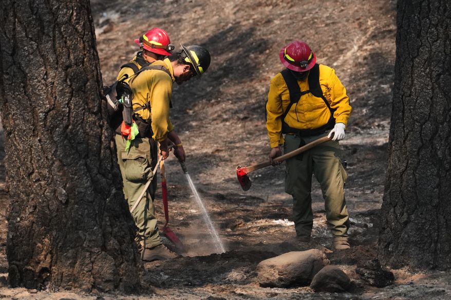 A crew does mop-up work in a burned area of Wyakin Park after a wildfire hit the northern part of Spokane, Wash., Tuesday, Aug. 4, 2026. (AP Photo/Lindsey Wasson)