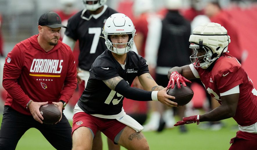 Arizona Cardinals quarterbacks Carson Beck, center, hands the ball off to Cardinals running back Trey Benson, right, as Cardinals offensive coordinator Nathaniel Hackett, left, looks on during NFL football training camp, Sunday, July 26, 2026, in Glendale, Ariz. (AP Photo/Ross D. Franklin)