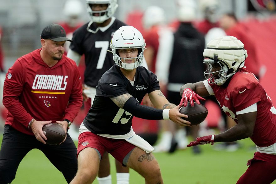 Arizona Cardinals quarterbacks Carson Beck, center, hands the ball off to Cardinals running back Trey Benson, right, as Cardinals offensive coordinator Nathaniel Hackett, left, looks on during NFL football training camp, Sunday, July 26, 2026, in Glendale, Ariz. (AP Photo/Ross D. Franklin)