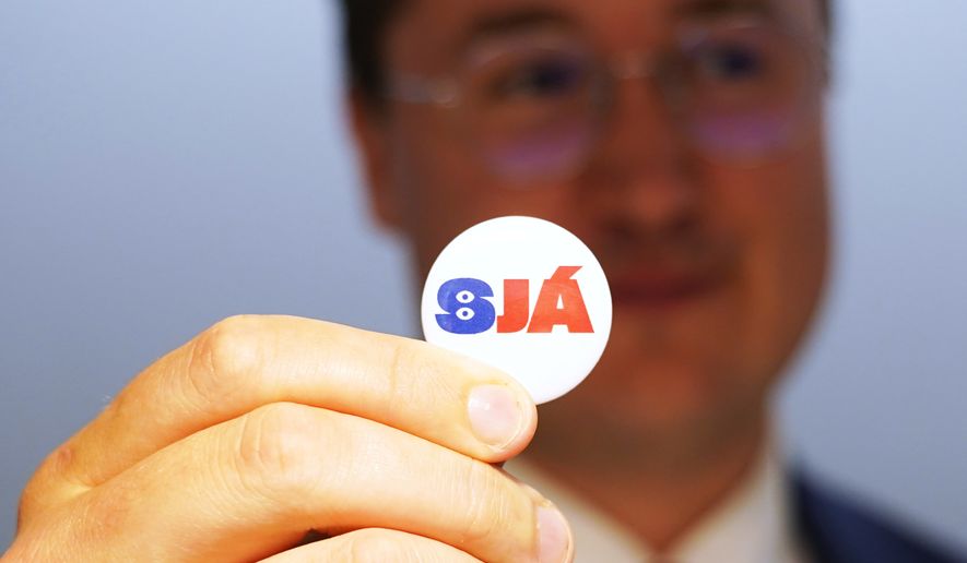 A man holds a badge reading "See", at the opening of the "Yes" campaign's office in Reykjavik, Iceland, Friday, Aug. 7, 2026. (AP Photo/James Brooks)
