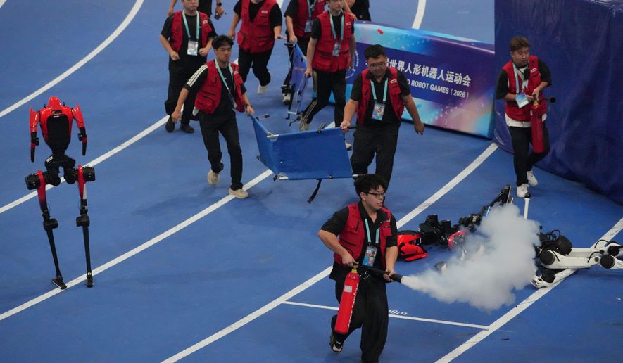 Officials extinguish a fire of a Humanoid robot after hitting the barrier at the end of the 100 meter final race during the World Humanoid Robot Games in Beijing, Wednesday, Aug. 26, 2026. (AP Photo/Achmad Ibrahim)
