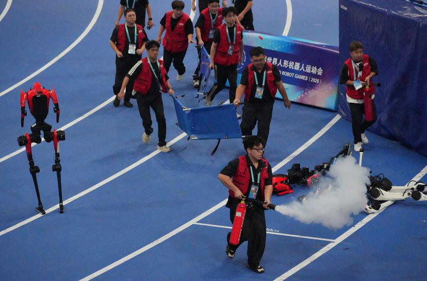 Officials extinguish a fire of a Humanoid robot after hitting the barrier at the end of the 100 meter final race during the World Humanoid Robot Games in Beijing, Wednesday, Aug. 26, 2026. (AP Photo/Achmad Ibrahim)