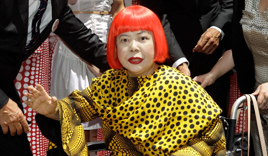 Japanese artist Yayoi Kusama waves in front of the windows of Vuitton's flagship store for the unveiling of a new collaborative collection by Kusama and Vuitton creative designer Marc Jacobs in New York, on July 10, 2012. (AP Photo/Kathy Willens, File)