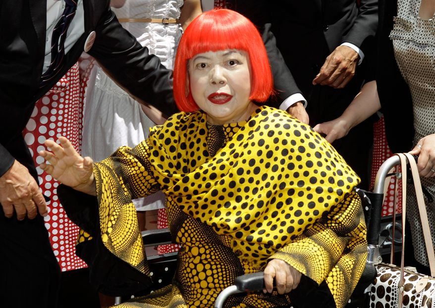 Japanese artist Yayoi Kusama waves in front of the windows of Vuitton's flagship store for the unveiling of a new collaborative collection by Kusama and Vuitton creative designer Marc Jacobs in New York, on July 10, 2012. (AP Photo/Kathy Willens, File)