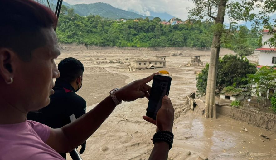 People take photographs and videos of the swollen, debris-choked banks of the Trishuli River after a flash floods in Nepal's Nuwakot district on Wednesday, Aug. 26, 2026. (AP Photo/Niranjan Shrestha)