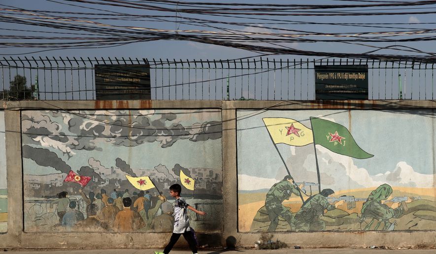 A boy walks past murals depicting Kurdish YPG and YPJ fighters battling Islamic State militants in Qamishli, northeastern Syria, Wednesday, Aug. 26, 2026. (AP Photo/Baderkhan Ahmad)