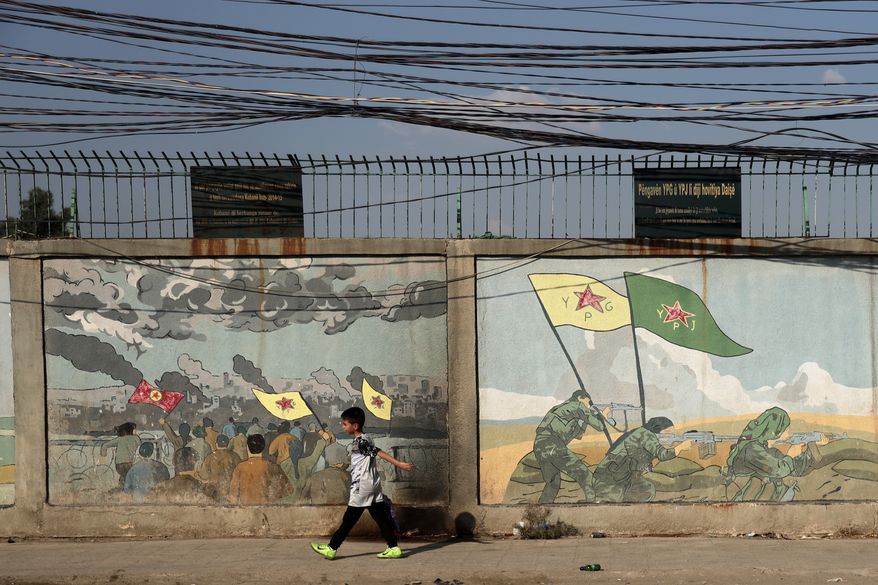A boy walks past murals depicting Kurdish YPG and YPJ fighters battling Islamic State militants in Qamishli, northeastern Syria, Wednesday, Aug. 26, 2026. (AP Photo/Baderkhan Ahmad)