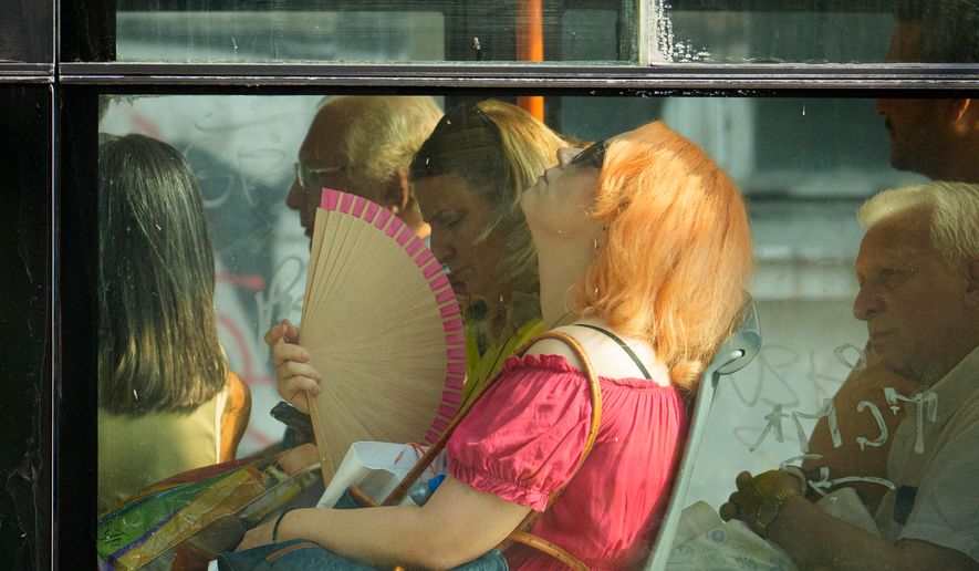FILE - A woman uses a fan to cool off while riding a bus on a hot day in Bucharest, Romania, Aug. 6, 2026. (AP Photo/Vadim Ghirda)