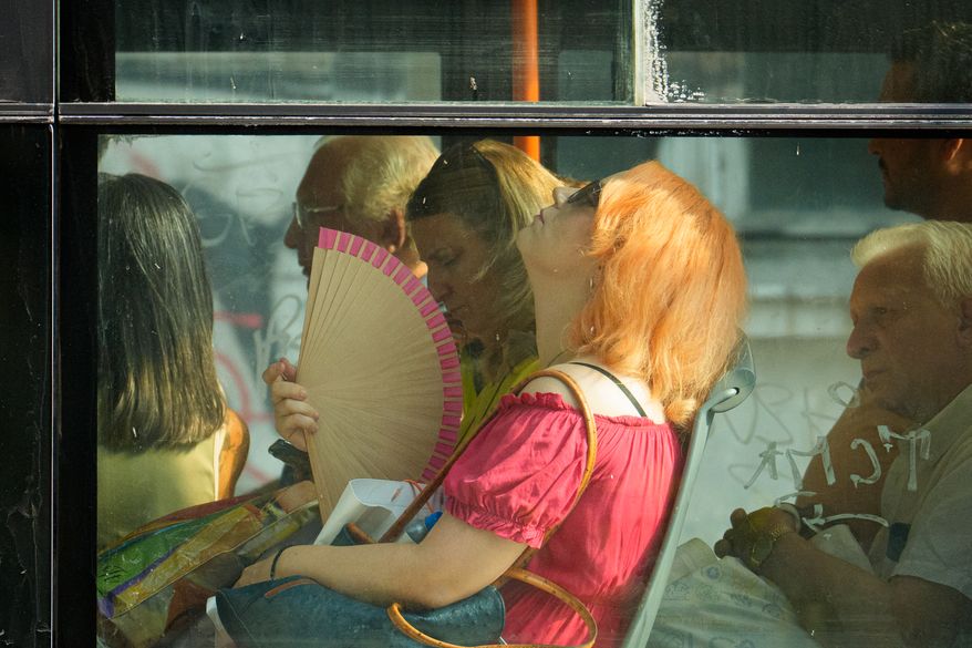 FILE - A woman uses a fan to cool off while riding a bus on a hot day in Bucharest, Romania, Aug. 6, 2026. (AP Photo/Vadim Ghirda)