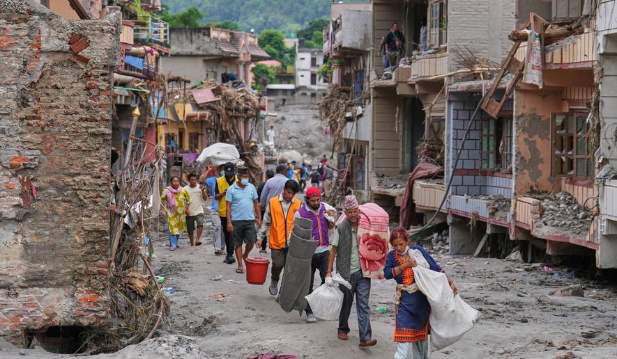 Residents carry their belongings salvaged from their damaged homes filled with mud and debris in Devighat, in Nepal's Nuwakot district, Saturday, Aug. 29, 2026, following the Aug. 26 flash floods. (AP Photo/Rajesh Kumar Singh)