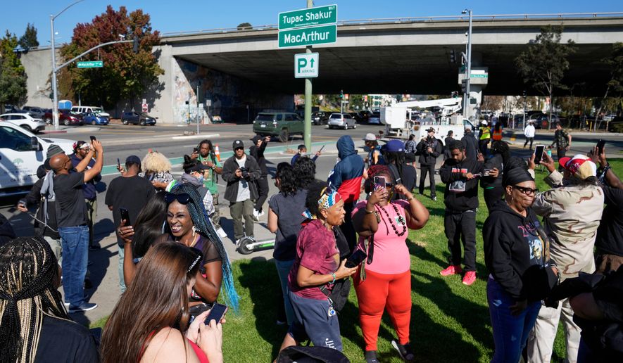 FILE - People take pictures and gather beneath a new sign during a street renaming ceremony for Tupac Shakur in Oakland, Calif., Nov. 3, 2023. (AP Photo/Eric Risberg, File)