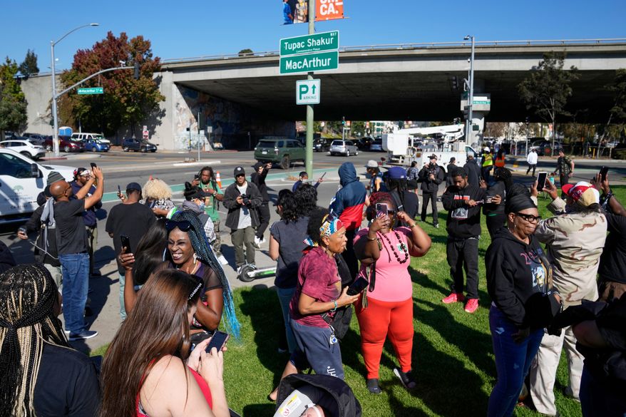 FILE - People take pictures and gather beneath a new sign during a street renaming ceremony for Tupac Shakur in Oakland, Calif., Nov. 3, 2023. (AP Photo/Eric Risberg, File)
