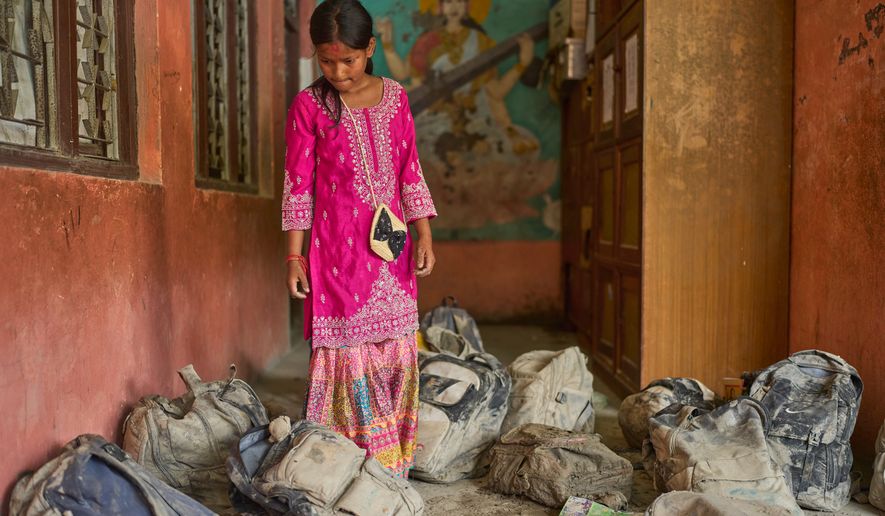 A student searches for her school bag from a pile extracted from the mud brought in by the recent flash floods, at the Shree Bagheswori Madhyamik School in Galchhi, Dhading district of Nepal Sunday, Aug. 30, 2026. (AP Photo/Niranjan Shrestha)