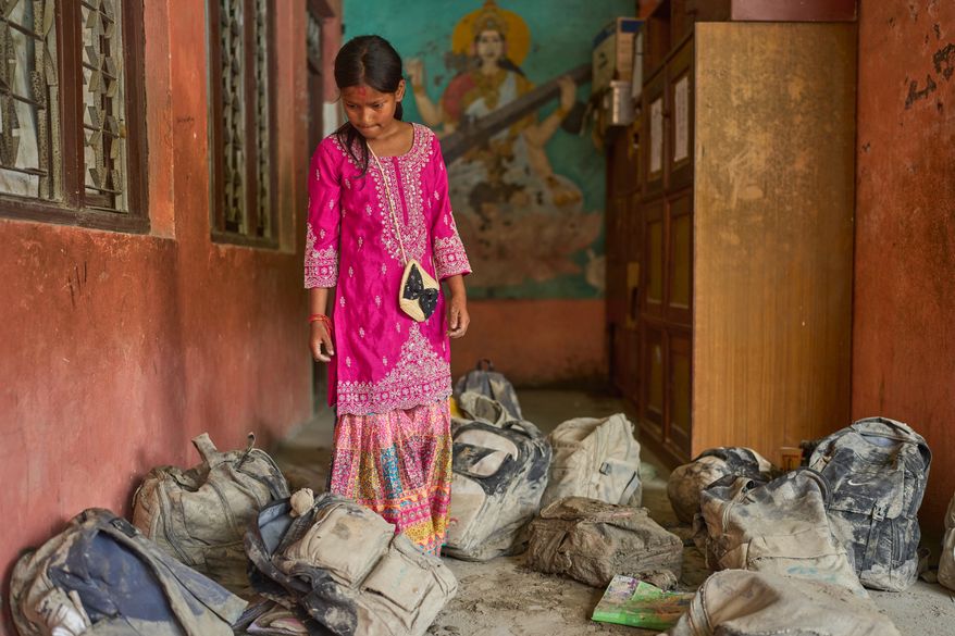 A student searches for her school bag from a pile extracted from the mud brought in by the recent flash floods, at the Shree Bagheswori Madhyamik School in Galchhi, Dhading district of Nepal Sunday, Aug. 30, 2026. (AP Photo/Niranjan Shrestha)