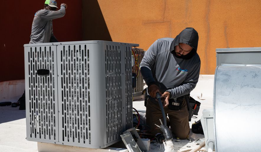 FILE - Sonel Telemaque, left, wipes sweat from his brow while installing a new air conditioning unit alongside Brian Hermosillo during record-breaking heat, March 19, 2026, in Tempe, Ariz. (AP Photo/Caitlin O'Hara, File)