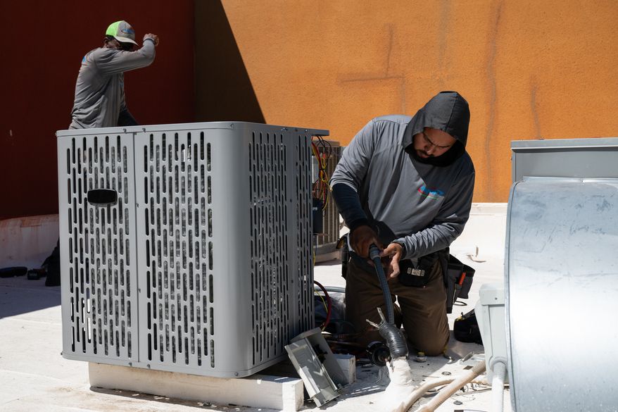FILE - Sonel Telemaque, left, wipes sweat from his brow while installing a new air conditioning unit alongside Brian Hermosillo during record-breaking heat, March 19, 2026, in Tempe, Ariz. (AP Photo/Caitlin O'Hara, File)