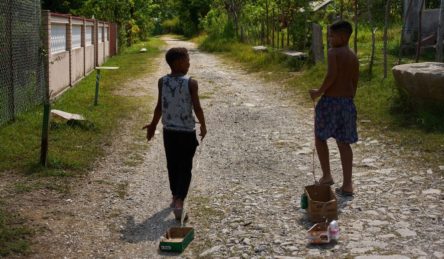 Children drag toys made from cardboard boxes as they walk in Minas, in Cuba's Havana province, Monday, Aug. 31, 2026. (AP Photo/Ramon Espinosa)