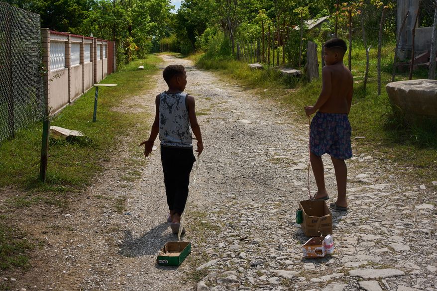 Children drag toys made from cardboard boxes as they walk in Minas, in Cuba's Havana province, Monday, Aug. 31, 2026. (AP Photo/Ramon Espinosa)