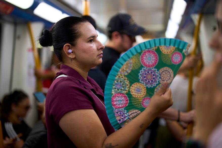 A woman uses a fan to cool herself on the subway in Madrid, Spain, on Aug. 18, 2026. (AP Photo/Manu Fernandez)