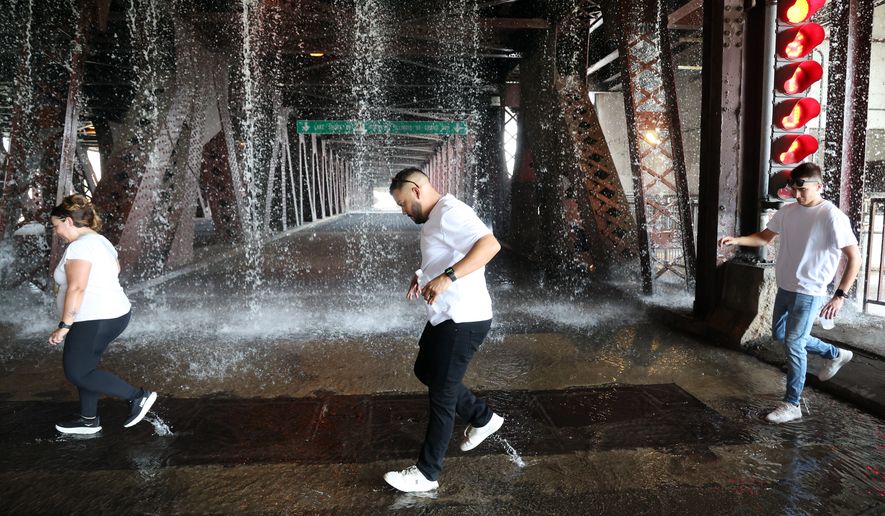 People scamper west across the lower level of the DuSable Lake Shore Drive bridge over the Chicago River on Wednesday, Sept. 2, 2026, as water pumped by a Chicago Fire Department boat flows down onto the double-leaf, double-deck, fixed counterweight bridge. (Terrence Antonio James/Chicago Tribune via AP)