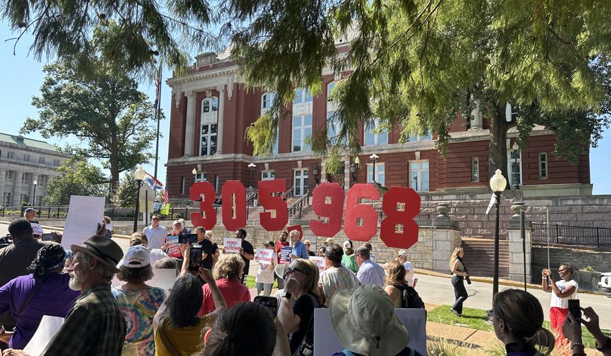 In this photo taken with a smartphone, people opposing a congressional redistricting plan rally outside the Missouri Supreme Court in Jefferson City, Mo., Wednesday, Sept. 2, 2026, while displaying the number of petition signatures submitted seeking a statewide vote on the measure. (AP Photo/David A. Lieb)