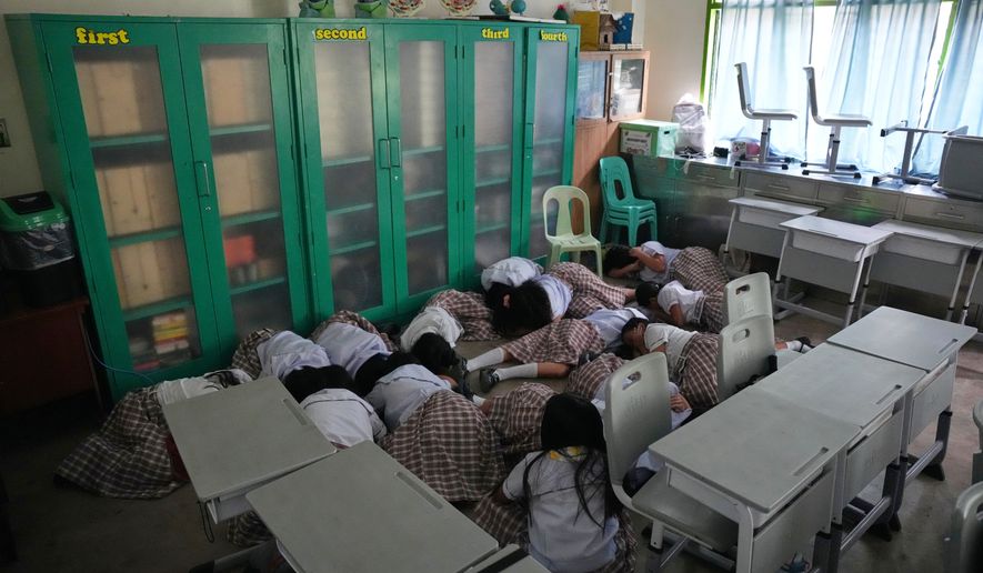 Students lay on the floor inside their classroom as they take cover during a nationwide school safety drill in San Rafael, Bulacan province, Philippines, Thursday, Sept. 3, 2026. (AP Photo/Aaron Favila)