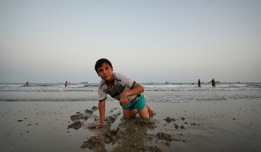 A boy plays in wet sand as others swim and commercial vessels lie anchored in the Strait of Hormuz off Bandar Abbas, Iran, Friday, Sept. 4, 2026. (AP Photo/Vahid Salemi)